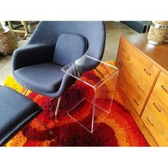 a chair and foot stool on a rug in a room with other furniture, including a dresser