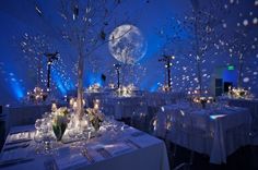 a room filled with lots of tables covered in white linens and decorated with trees