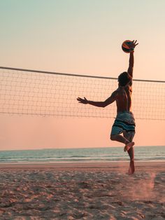 a man jumping up to hit a volleyball on the beach