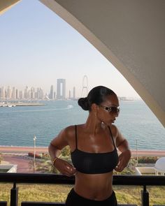 a woman standing in front of a window looking out at the water and cityscape