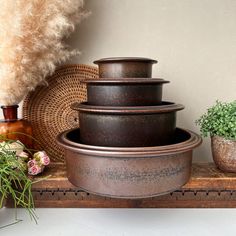 a stack of pots sitting on top of a wooden shelf next to a potted plant