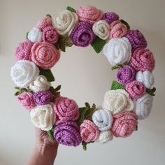 a hand holding a crocheted wreath with pink, white and purple flowers on it