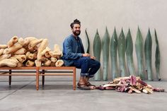 a man sitting on a bench next to a pile of bananas and other fruit items