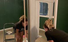 two women are painting a room with green walls