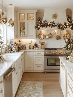 a kitchen decorated for christmas with white cabinets and gold trimmings, lights and garland