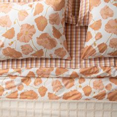 an orange and white flowered comforter with two pillows on it's side