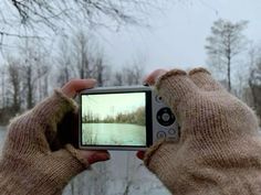 someone taking a photo with their cell phone in the winter time snow covered trees and water behind them