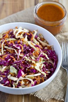 a white bowl filled with coleslaw next to a fork and spoon on top of a wooden table