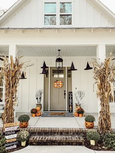 a white house decorated for halloween with pumpkins on the porch and corn stalks in front