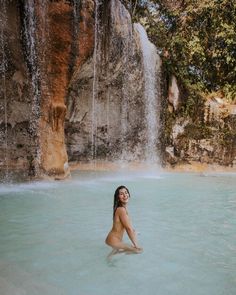 a woman is sitting in the water near a waterfall