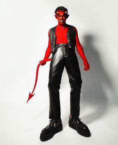 a man in red shirt and black pants with devil makeup on his face standing next to a white wall