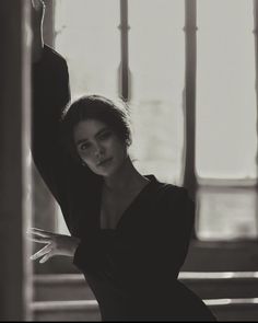 a black and white photo of a woman leaning against a wall with her arm in the air