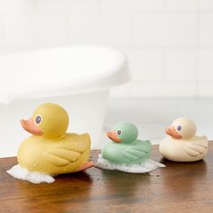 three rubber ducks sitting on top of a wooden table next to a bath tub in a bathroom