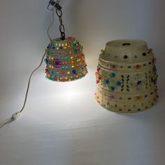 two lamps that are sitting next to each other on a white surface, one is turned on and the other has beads