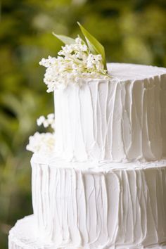 a three tiered cake with white flowers on top and greenery in the background