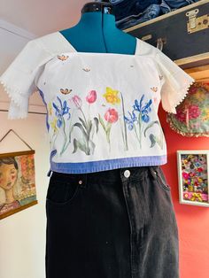 a woman's white top with colorful flowers painted on it and black skirt underneath