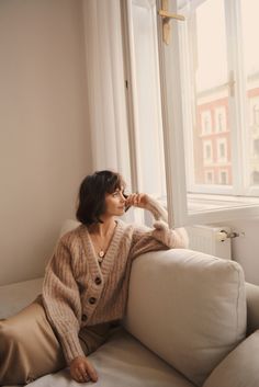 a woman sitting on top of a white couch next to a window with windowsills