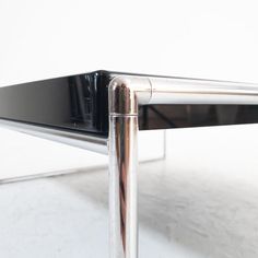 a close up of a metal table with a glass top and chrome legs on a white surface