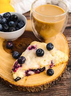 a piece of blueberry cheesecake sitting on top of a wooden plate next to a cup of coffee