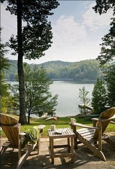 two wooden chairs sitting on top of a sandy beach next to a body of water