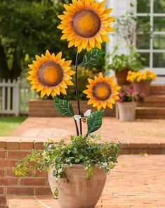 three large sunflowers in a pot on the ground near some steps and trees