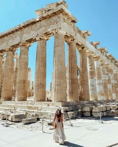 a woman standing in front of an ancient building with columns and pillars on the sides