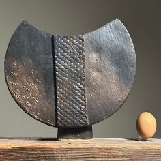 an egg sitting on top of a wooden table next to a piece of metal art