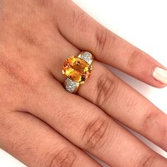 a woman's hand with an orange and white diamond ring on top of it