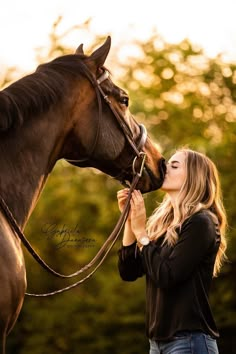 a woman is kissing her horse while she stands in front of the tree's