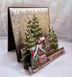 a christmas card with snow covered trees and houses on the front, sitting on a table