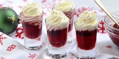 three glasses filled with red liquid and whipped cream on top of a white table cloth