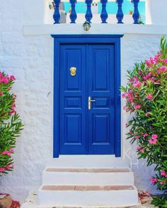 a bright blue door sits in front of a white building with pink flowers on the steps