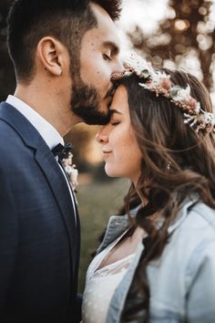 a man in a suit and tie kissing a woman with a flower crown on her head