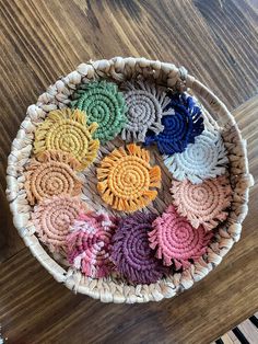 a wicker basket filled with colorful crochet flowers on top of a wooden table