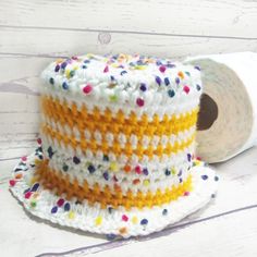 a crocheted hat with sprinkles on it next to a roll of toilet paper