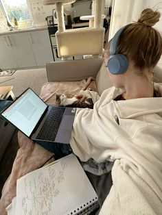 a woman with headphones on laying in bed next to a laptop computer and cat