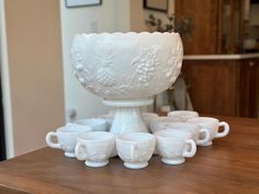 a white bowl sitting on top of a wooden table next to cups and saucers