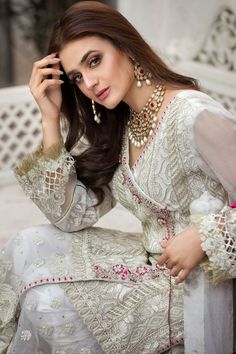 a woman sitting on top of a white bench wearing a dress and holding a cell phone to her ear