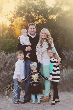 a family posing for a photo in front of some bushes and trees with the sun behind them