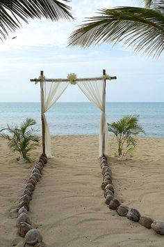 an arch made out of rocks on the beach with a white cloth draped over it