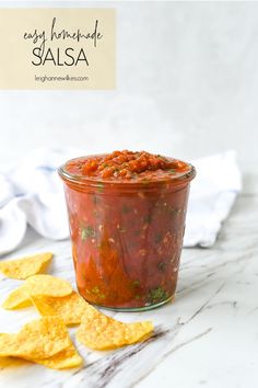 salsa in a glass jar with tortilla chips on the side next to it