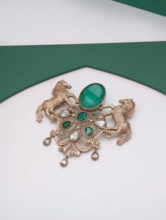 The "Roshan-e-Sawaar Brooch" is an enchanting ode to untamed beauty. This captivating accessory showcases two intricately designed galloping horses, adorned with four stunning green gemstones that exude elegance and vitality. The Glitter Horse Brooch captures the untamed grace and boundless energy of these majestic creatures, empowering every modern individual to embrace their inner strength and free spirit. With its dazzling beauty and symbolic significance, this brooch is the perfect statement Gold Brooch For Men, Antique Wedding Brooch With Intricate Design, Ornate Wedding Brooch With Intricate Design, Ornate Wedding Brooches With Intricate Design, Heirloom Wedding Brooches With Intricate Design, Victorian Brooch Jewelry For Wedding, Victorian Brooch For Wedding, Ornate Wedding Brooch Jewelry, Victorian Wedding Brooch Jewelry