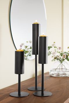 two black candle holders on a table with a mirror in the background