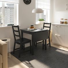 a kitchen table with two chairs and a clock on the wall above it in front of a window