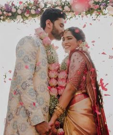 a man and woman standing next to each other under a flower covered arch with petals