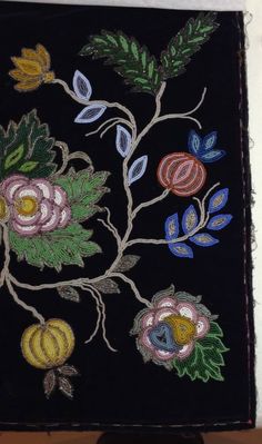 an embroidered piece with flowers and leaves on a black background, sitting on a table