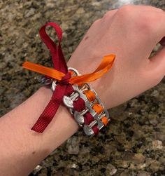 a person's hand with an orange and red ribbon on it that is attached to a silver bracelet