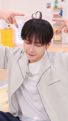 a man with black hair sitting on top of a bed holding his hand up to his head