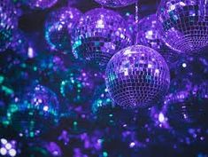 many shiny disco balls are hanging from the ceiling in purple and green colors with lights shining on them