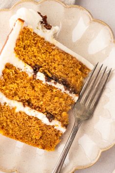 a piece of carrot cake with white frosting on a plate next to a fork